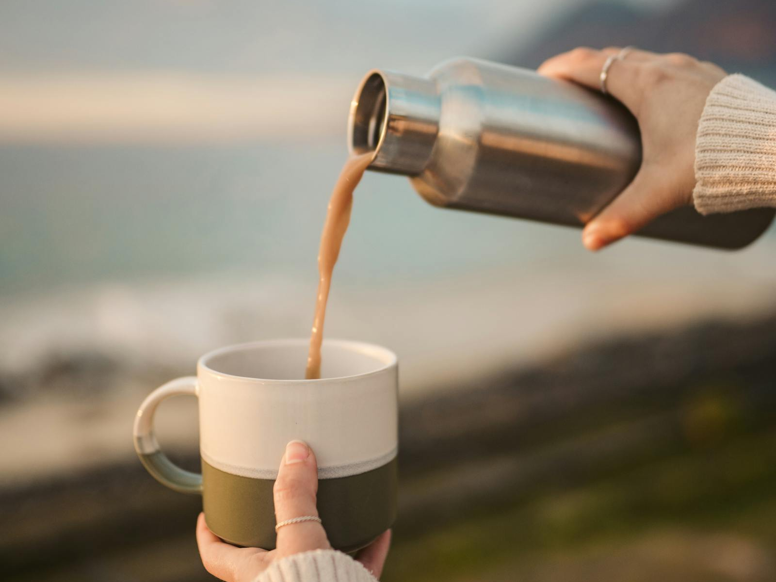 Hot coffee poured from an insulated travel bottle into a morning mug